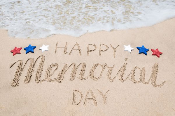 Happy Memorial Day written in the sand at the beach with water coming ashore